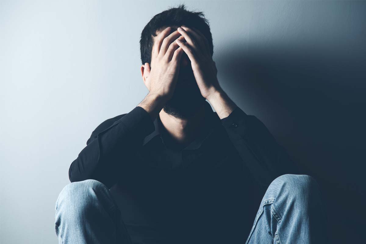 man sitting against wall with hands covering face wondering What is TMS Therapy for Depression