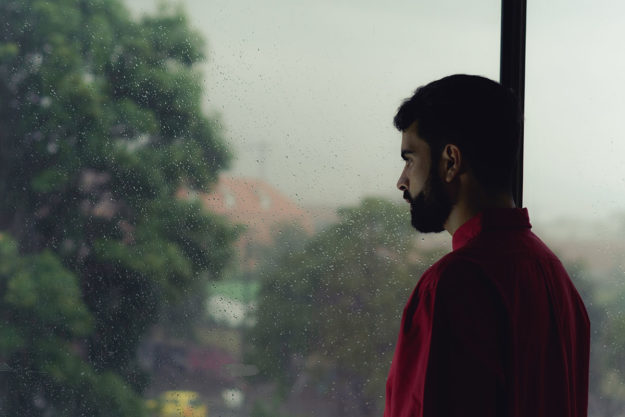 man looking out window at city wondering What is TMS Therapy for Anxiety