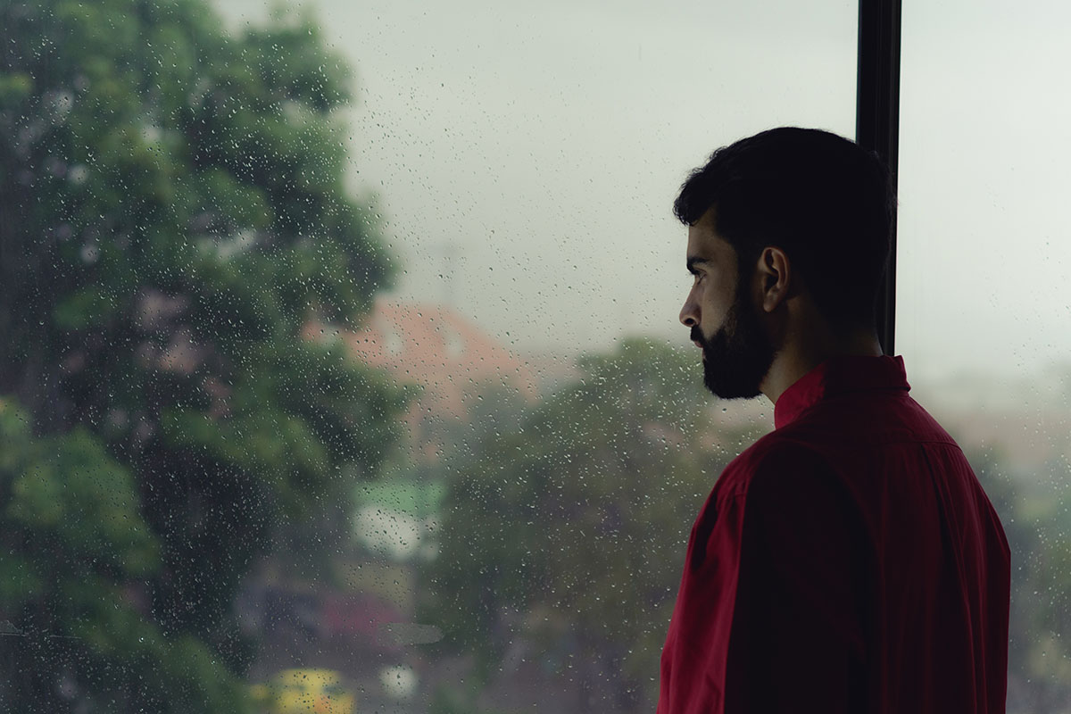 man looking out window at city wondering What is TMS Therapy for Anxiety